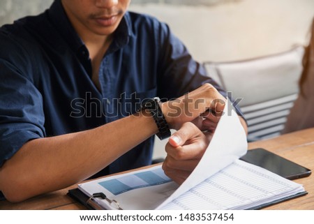Worker checking time and looking at wrist watch at home office. Young Businessman seeing clock to work. On desk with calendar, annual, and summary report.Time out for appointment meeting concept.