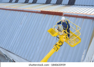 Worker In Cherry Picker Above Warehouses