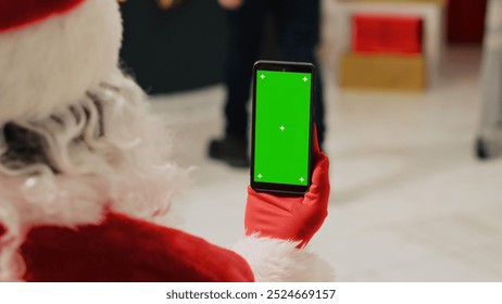 Worker in Christmas ornate clothing store dressed as Santa Claus holding green screen smartphone, browsing through fashion shop ecommerce website, inputting promotional holiday sales online - Powered by Shutterstock