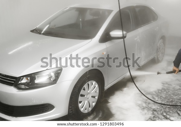 Worker cleaning automobile with\
high pressure water jet at car wash. washing machine with\
foam
