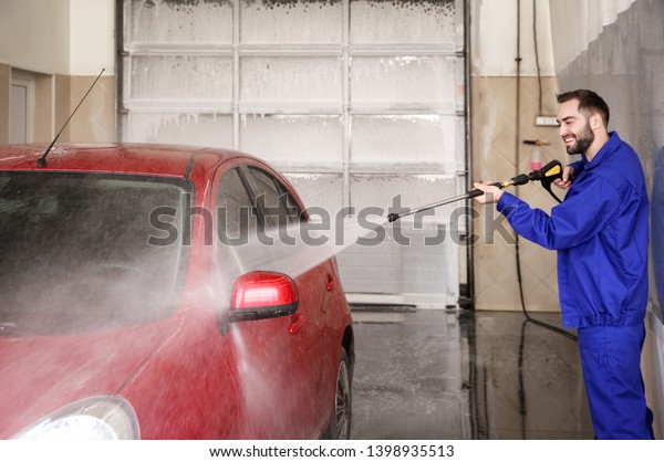 Worker cleaning automobile with high pressure water\
jet at car wash