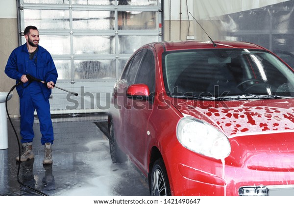 Worker cleaning automobile with high pressure water\
jet at car wash