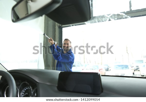 Worker cleaning automobile\
windshield with high pressure water jet at car wash, view from\
inside