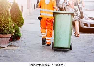 Worker of cleaning company in orange uniform with a green garbage bin