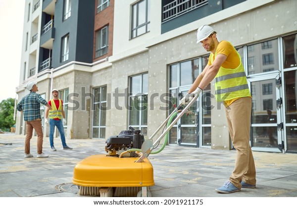 Worker cleaning construction site and two men\
near building