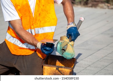 Worker Cleaning A Dirty Trowel With Sponge From Rubber Granules (rubber Mulch). 