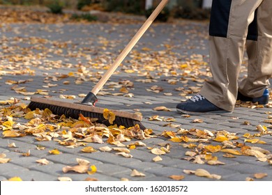 Worker Cleaning Up The Driveway From Autumn Leaves