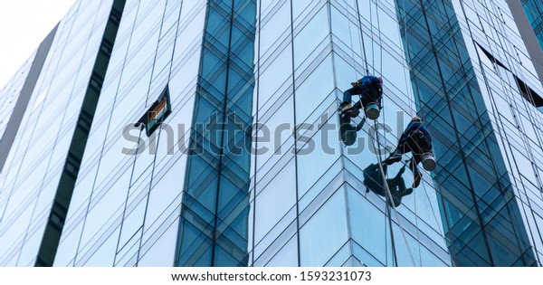 Worker cleaning glass curtain wall\
at high rise building with rope. Special Job\
concept.
