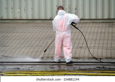 Worker cleaning with high-pressure cleaner railways in port