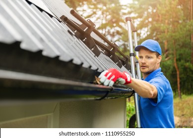 worker cleaning house gutter from leaves and dirt