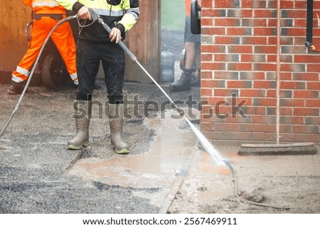 Worker cleaning a path surface with high-pressure water in a construction area during daylight hours