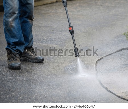 Worker cleaning pavement using an electric water blaster.