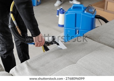 Worker cleaning sofa upholstery with extraction machine and nozzle. Deep cleaning process removes dirt and stains, ideal for residential cleaning service promotion and maintenance.