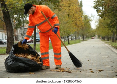 Worker cleaning street from fallen leaves on autumn day