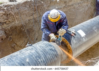 Worker is cleaning welding seam on pipeline with a grinding machine. Preparation for welding