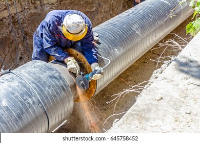 Worker is cleaning welding seam on pipeline with a grinding machine. Preparation for welding