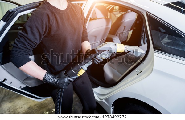 Worker cleans car\
interior with vacuum\
cleaner