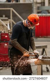 Worker cleans metal part using grinding machine in metalworking workshop.