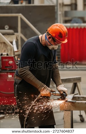 Worker cleans metal part using grinding machine in metalworking workshop.
