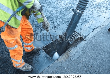 Worker cleans storm drain to remove debris and improve water flow in urban area during daytime operations