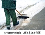 Worker clearing snow from sidewalk during blizzard, clean walkway. Utility worker shoveling snow on city street. Man clearing snowy walkway with shovel. Snow removal work, ensuring pedestrian safety