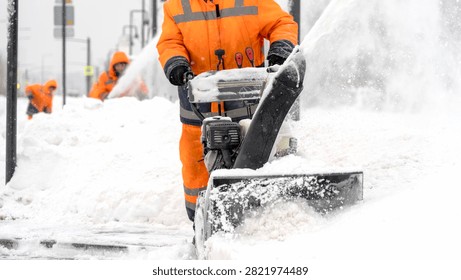 Worker clears snow with machine. Snow flurries fly as path clears. Winter streets require urgent care. Worker focused on job. Efficiency in harsh weather. Ideal for winter maintenance scenes
