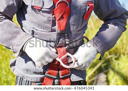 worker climber preparing for steeplejack work. climber tightens the safety belt and check fixing and carbines. closeup