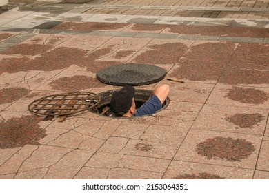 A worker climbs out of an open manhole in the road. Dangerous open unprotected manhole on the road. Accident with a sewer manhole in the city. The concept of repairing underground utilities.