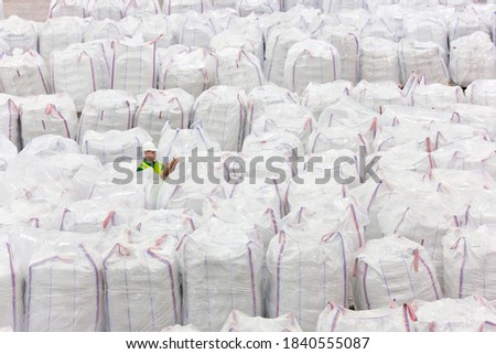 Worker with clipboard among large bags of plastic pellets in warehouse inspecting the bags
