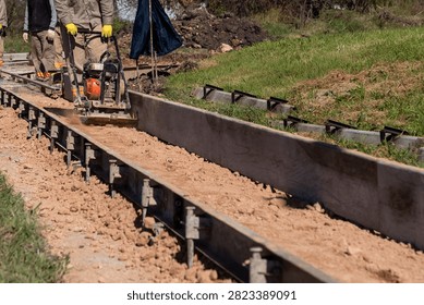 Worker compacting soil subbase with plate compactor between metal formwork for curb construction