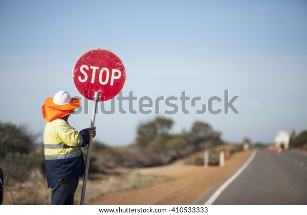 The worker construction hand hold circle red road stop\
sign held at side country highway road landscape in Australia road\
maintenance Vintage Tone. Careful Keep slow down Traffic control.\
Man. 