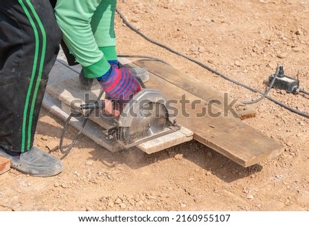 Worker contractor using circular saw to cut formwork boards on a new building constructiion project