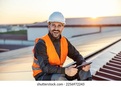 Worker controlling solar panels over tablet and smiling at the camera.
