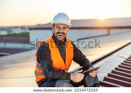 Worker controlling solar panels over tablet and smiling at the camera.