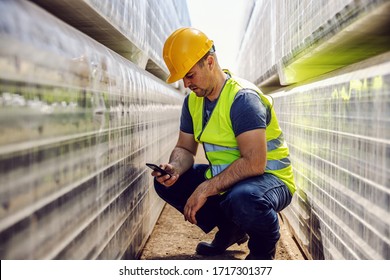Worker crouching between pile of folded bricks and using smart phone.