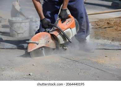 A worker cuts asphalt with a circular saw at a construction site, highway construction.