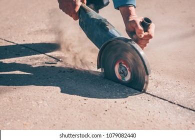 The worker cuts the asphalt layer with an angle grinder with a diamond disc