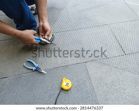 A worker cuts galvanized wire mesh outdoors in daylight using an angle grinder to size the metal sheet for a DIY construction project