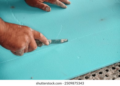 Worker cutting blue polystyrene foam heat insulation with old retractable utility knife, closeup detail - Powered by Shutterstock