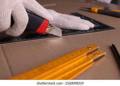 Worker Cutting Cardboard With Utility Knife And Ruler, Closeup