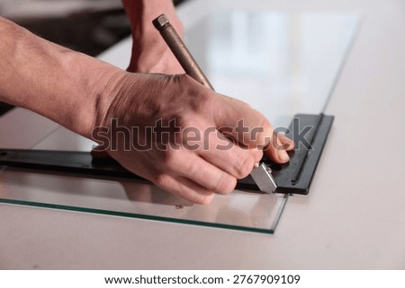 Worker cutting glass sheet at table in workshop, closeup