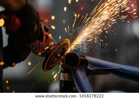 Worker cutting, grinding and polishing motorcycle metal part with sparks indoor workshop, close-up.
