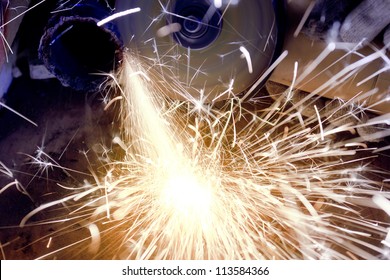Worker cutting metal using angular grinding machine, orange flying sparks