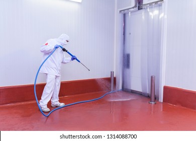 worker of the cutting room washing the cold room with water pressure equipment and dressed in hygienic clothing