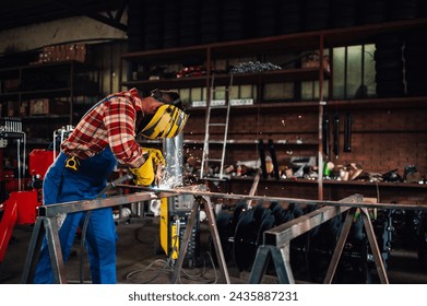 Worker in a dangerous work environment welding metal while wearing a safety equipment and looking down at the flying sparks. Blurred background of a working space and shelves with tools.Copy space.