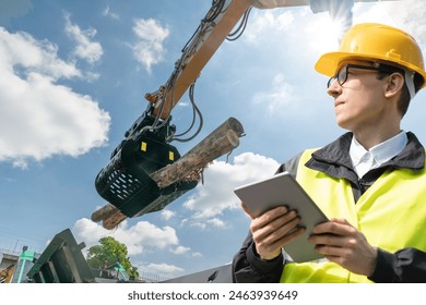 Worker with digital tablet controls process of loading timber	