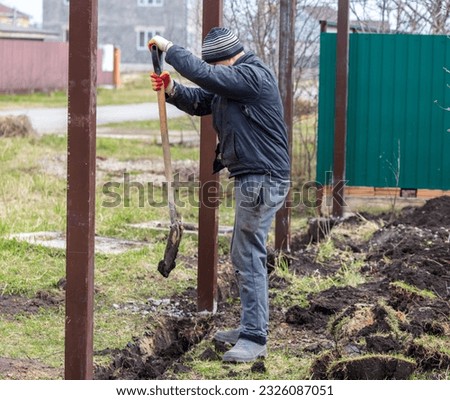 A worker digs the ground with a shovel to install a fence.