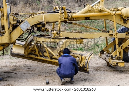 Worker doing adjustments of motor grader at construction site