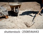 A worker doing paving work throws soil into a construction wheelbarrow with a shovel in his hand. The process of laying paving stones on the pavement.