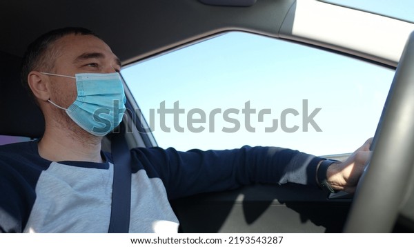 worker driver in mask in the coronavirus pandemic.
delivery service. delivery of goods concept. man driver in a
protective mask rides a car on the road. Food delivery delivery
travel service worker